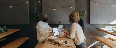 Drei Menschen sitzen mit Masken um einen Tisch