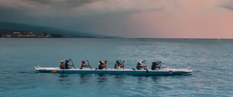 People rowing in front of lilac sky