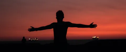 Silhouette eines Menschen im Sonnenuntergang mit ausgestreckten Armen