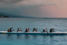 People rowing in front of lilac sky